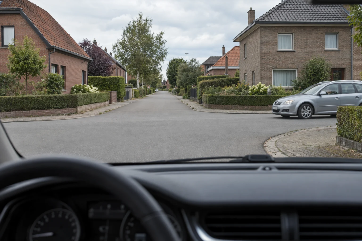 Driver's view of a Belgian residential junction without signs or signals: a car is arriving from the right.