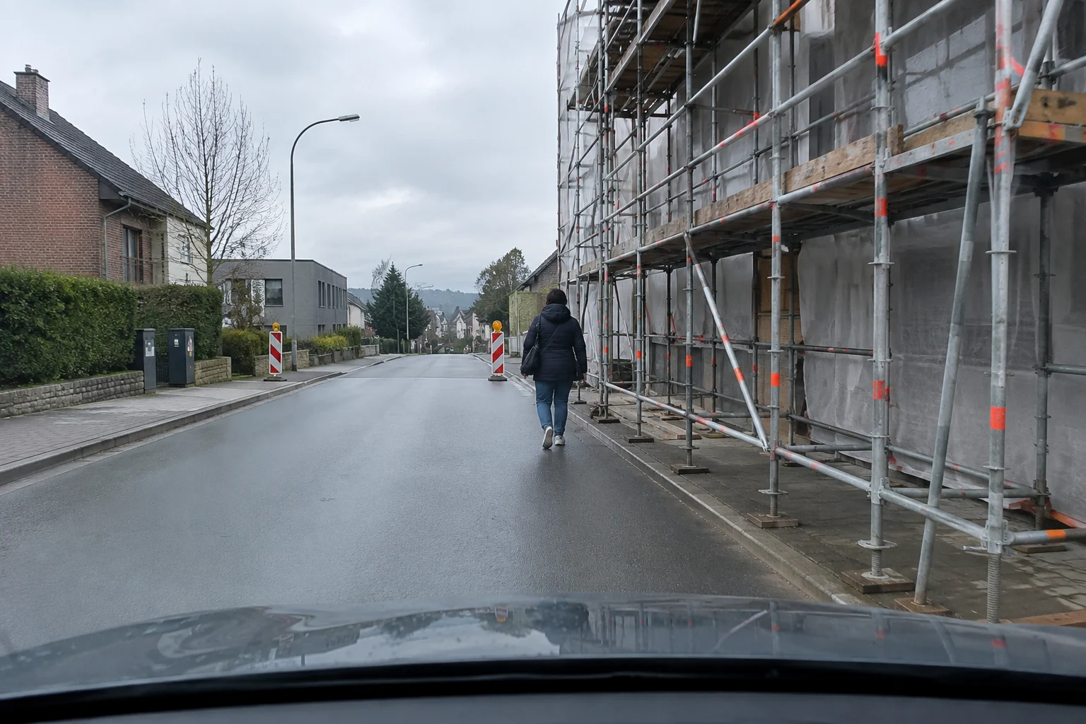 Image originale Tout pour mon permis (générée par IA, panneaux officiels) Rue étroite dont le trottoir est occupé par un échafaudage ; un piéton marche sur la chaussée.